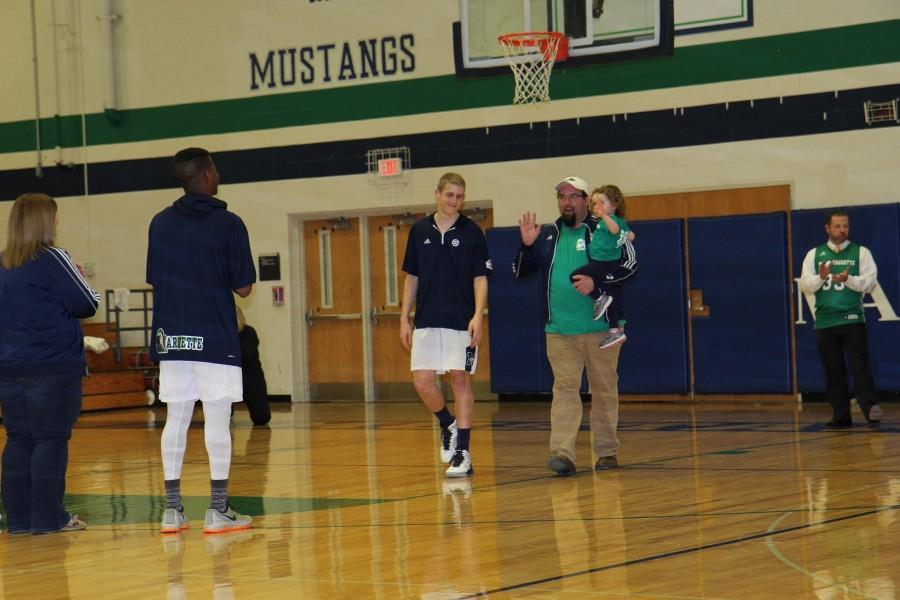 Paul Myers, junior, walks Kevin Sansom, physics teacher, up the court for the teacher appreciation ceremony before the game Tuesday, Feb. 9. Each player chose a faculty member to recognize before the game. Mr. Sansom is a fun teacher who is dedicated in helping his students succeed, Myers said. 