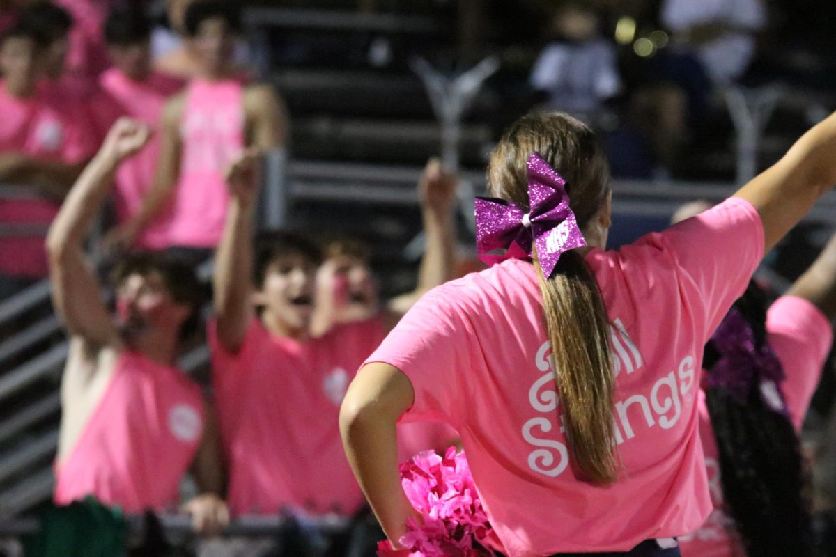 Sydney Vaccaro, junior, cheers while the Stang Gang yells in the background at the Friday, Sept. 8, game against Hazelwood Central. The Color Out shirts sold for $5 featured a retro font and pink color inspired by the popularity of the Barbie movie.