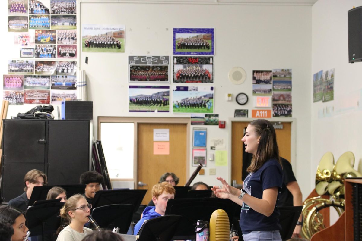 Kaylin Knost, band director, directs her sixth hour class with images of previous bands in the background. Knost is the daughter of MHS first Teacher of the Year and former Superintendent Dr. Eric Knost, who was the bands first director.