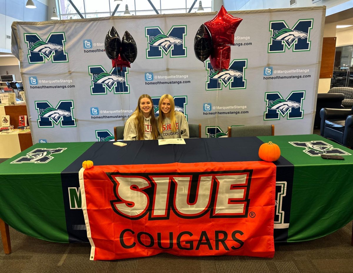 Carle Bachman, senior, poses with sophomore Ellie Pagan (left). Friends and family decorated the table with balloons and flags to commemorate her signing.