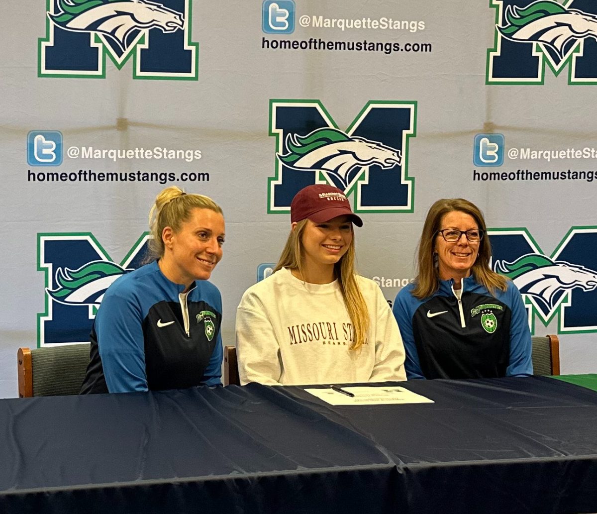 Bri Kappeler, senior, is joined by MHS soccer coaches Jenna King (left) and Shawn McAteer (right) in the library to celebrate Winter Signing Day. 