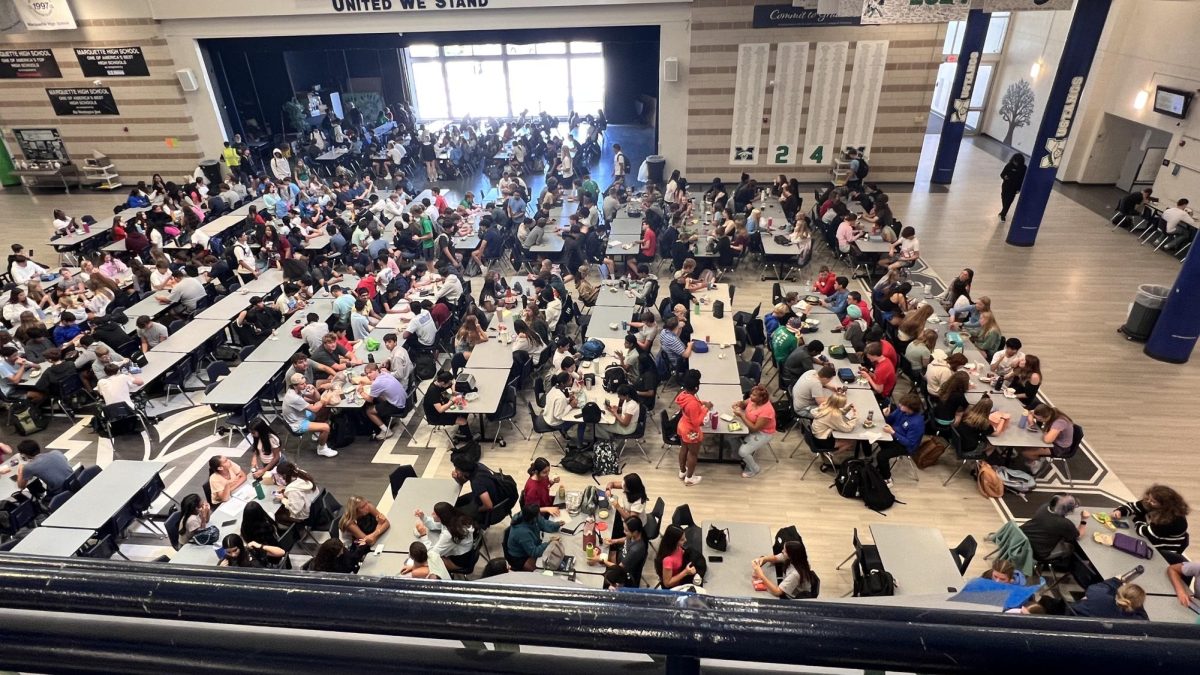 Students eat lunch during the first lunch period. The cafeteria added five new tables on the commons stage to accommodate the larger number of students in each lunch.