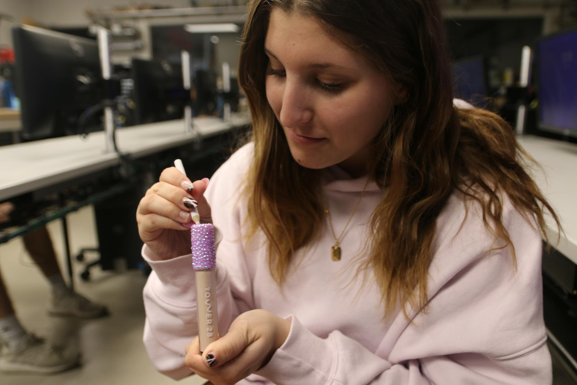 Lyla Sherman, junior, bedazzles her Tower 28 concealer with a wax-tipped pen. Though bedazzling has existed for decades, it has recently become more popular due to social media. 