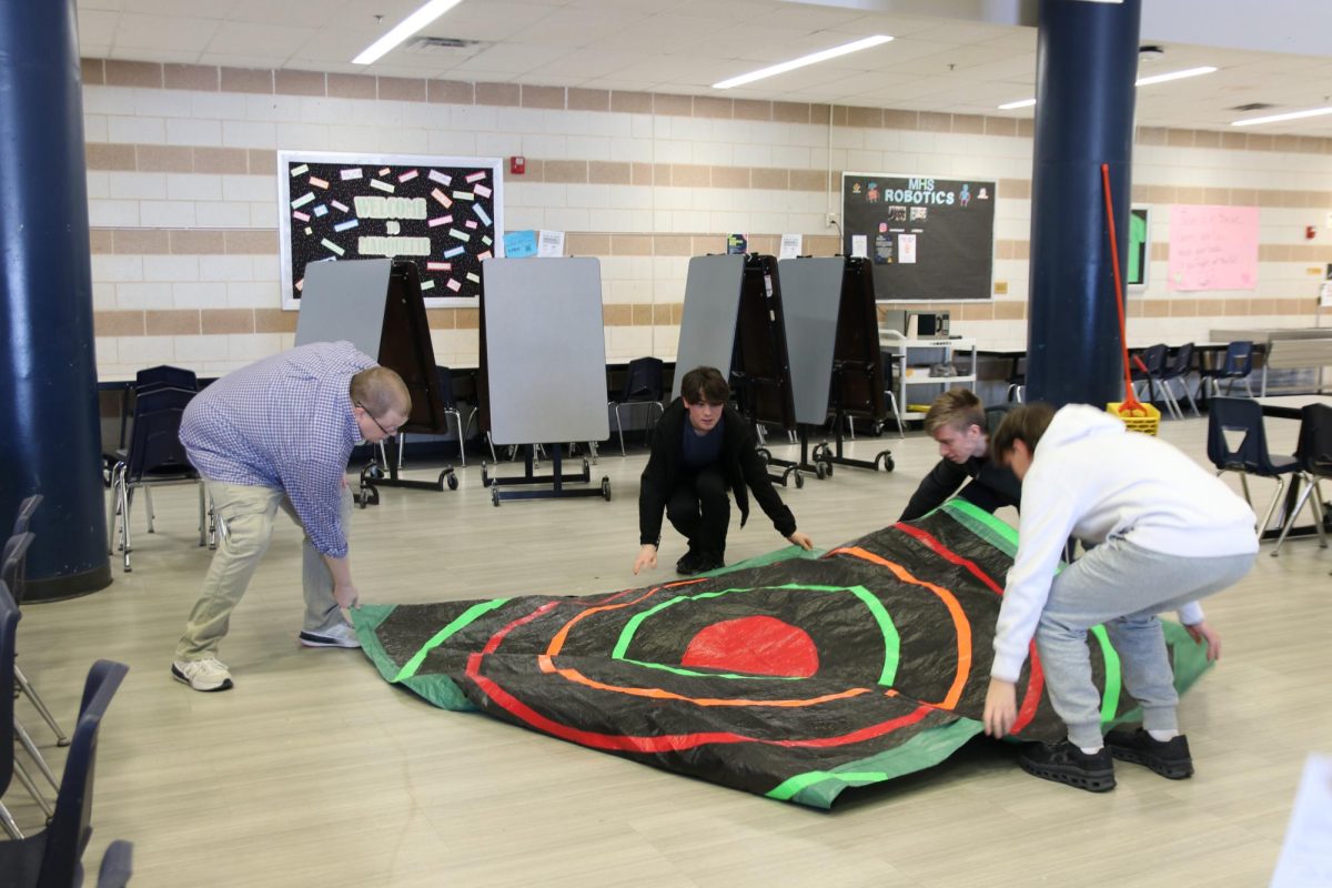 Mike Wagner, science teacher, and juniors Gavin Park, Nathan Baldus and Hudson Williams set up the Bullseye for the seventh hour AP Physics 1 egg drop lab on Thursday, Feb. 26. Students were tasked with creating a delivery system that would protect an egg from cracking when dropped from the third floor to test their abilities of understanding impulse momentum theorem. 