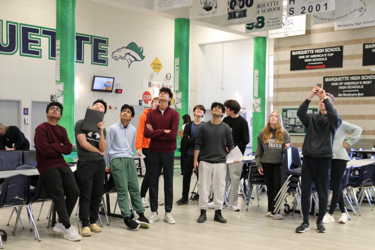 Students watch as a delivery system falls from the third story. Before designing their projects, students voted on what three materials they wanted to use, in addition to the materials that were already given, which consist of computer paper, masking tape and string. After working on their delivery systems, students were able to test them. 