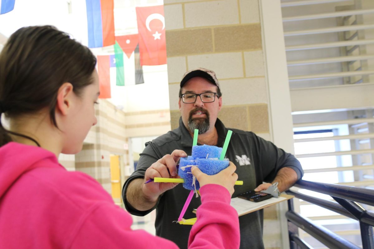 Adam Sansom, science teacher, and Gabriella Silasi, junior, discuss how compressible the pool noodle foam of her delivery system is. Sansom explains that falling from the third story might have hit the delivery system hard enough to compress the form and increase the time of collision, which lowers the average force exerted on her egg, causing it to be more likely to survive.